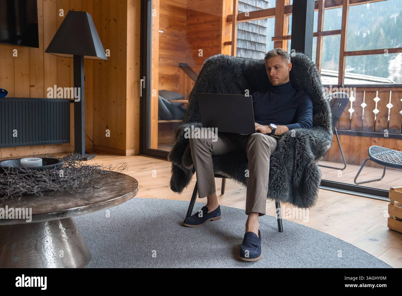 Mann, der an einem Laptop in einem luxuriösen Chalet in den italienischen Alpen arbeitet Stockfoto