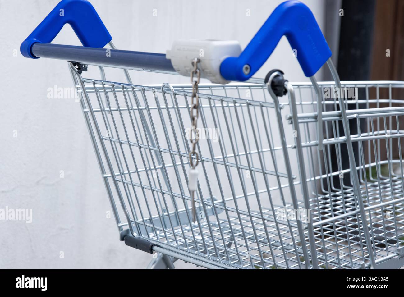 Verlassener verlassener leerer Einkaufswagen aus Metall mit blauem Griff, der im Hinterhof des Ladens an der schmutzigen Betonwand an der Kopfsteinpflasterstraße stand. Fragment, Beschneidung Stockfoto