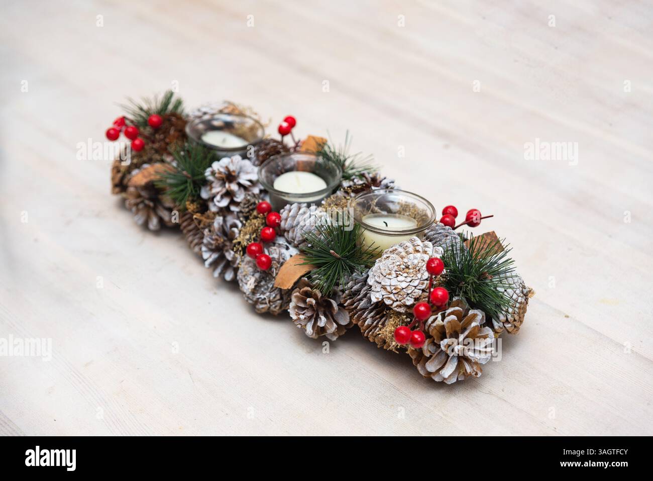 Dekoratives Herzstück der Feiertage mit Tannenzapfen, roten Beeren, immergrünen Zweigen und Teelichtkerzen für festliche Tischdekoration. Stockfoto