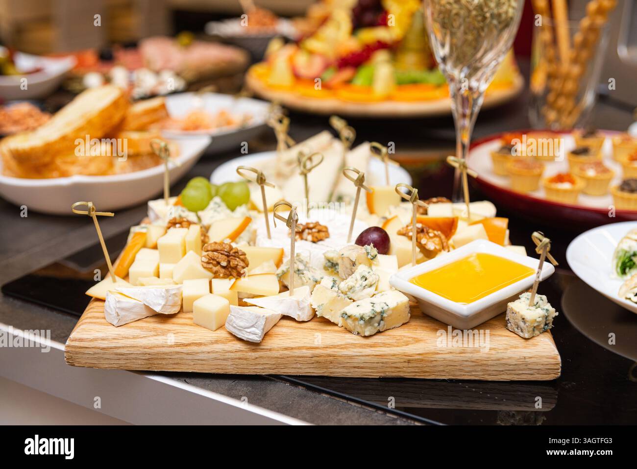Elegante Käseplatte mit verschiedenen Käsesorten, Walnüssen, Trauben und Honig-Dip, perfekt für Partys oder Weinpaare. Stockfoto