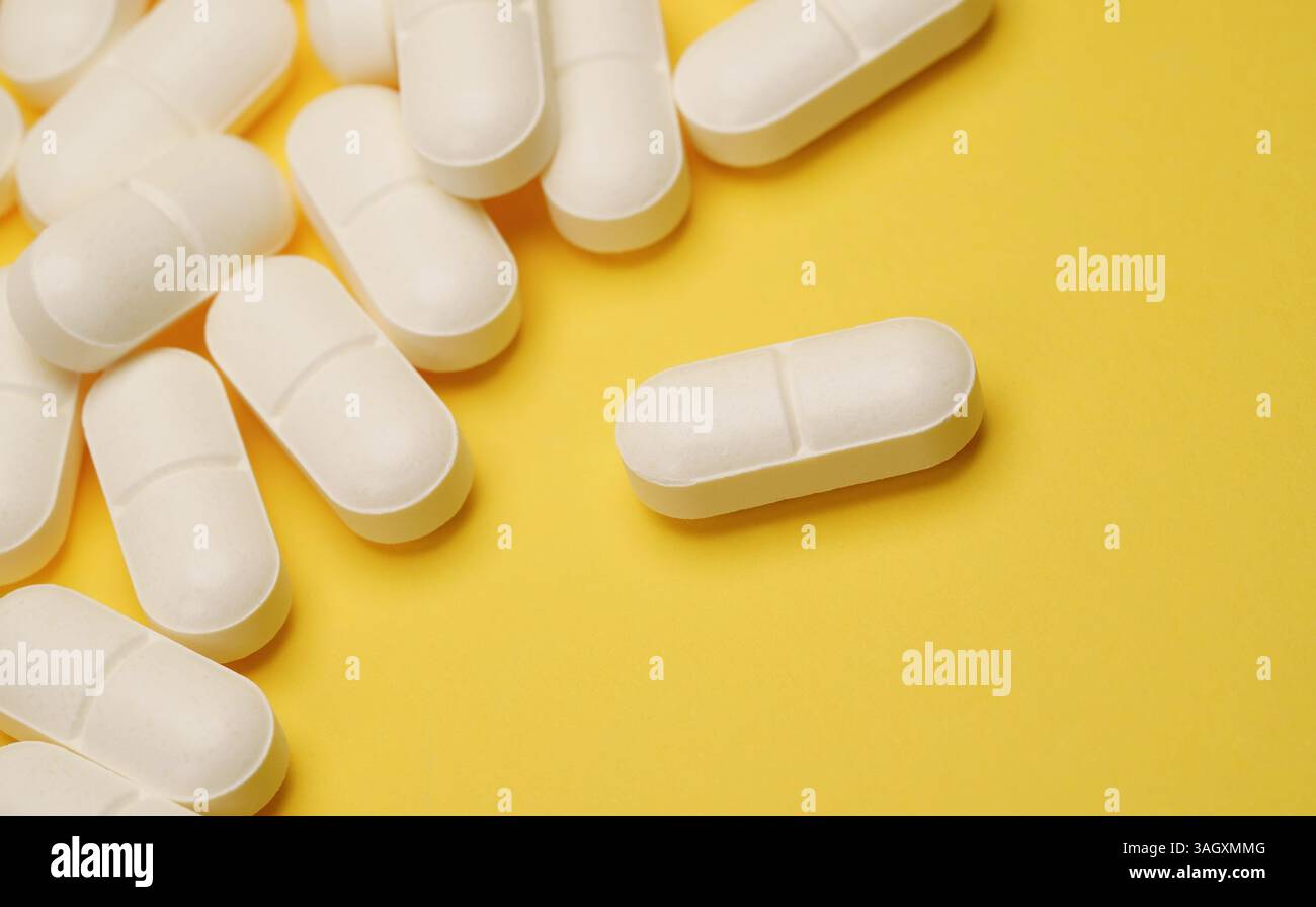 Arzneimittelpillen medizinisches und pharmazeutisches Konzept mit Nahaufnahme weißer Pillen auf gelbem Hintergrund. Stockfoto