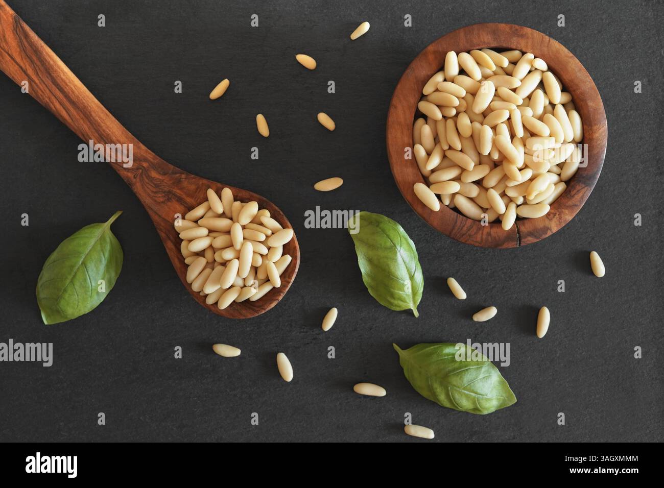 Pinienkerne über dem Kopf mit einer Nahaufnahme von oben auf viele schalen Pinienkerne in einem Holzlöffel und in einer Schüssel auf einem dunkelgrauen Hintergrund. Stockfoto