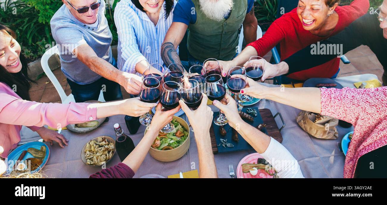Fröhliche Familie jubelt mit Rotwein beim Barbecue-Abendessen im Freien zu Hause - verschiedene Altersstufen der Menschen, die Spaß am Wochenendmahl haben - Essen, Geschmack und Sommer c Stockfoto