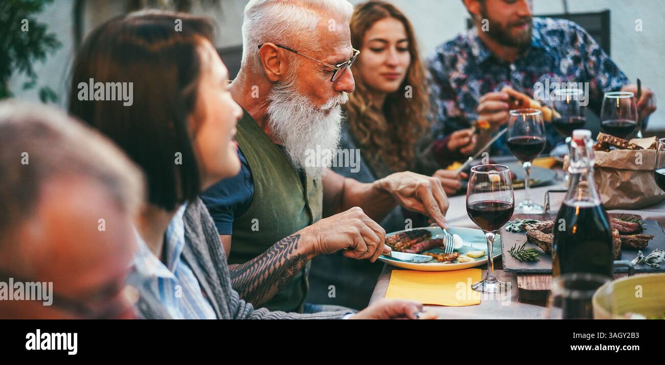Fröhliche Familienmitglieder, die Spaß beim Barbecue-Abendessen haben - multirassische Freunde essen beim bbq-Essen - Essen, Freundschaft, Treffen und Sommer-Lifestyle-Konzept Stockfoto