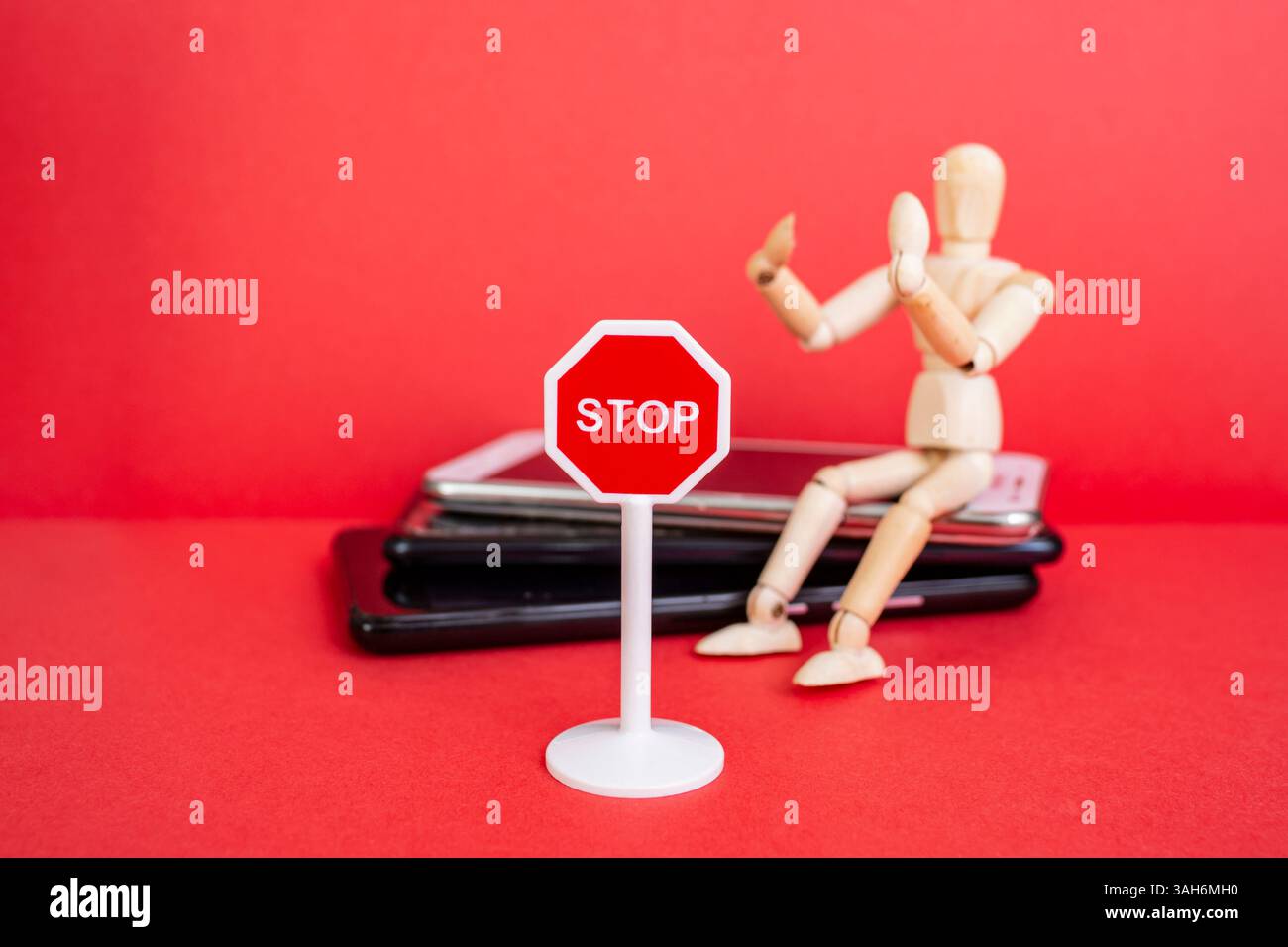 Hölzerne Schaufensterpuppe auf einem Smartphone-Stapel mit einem Stoppschild auf rotem Hintergrund Stockfoto