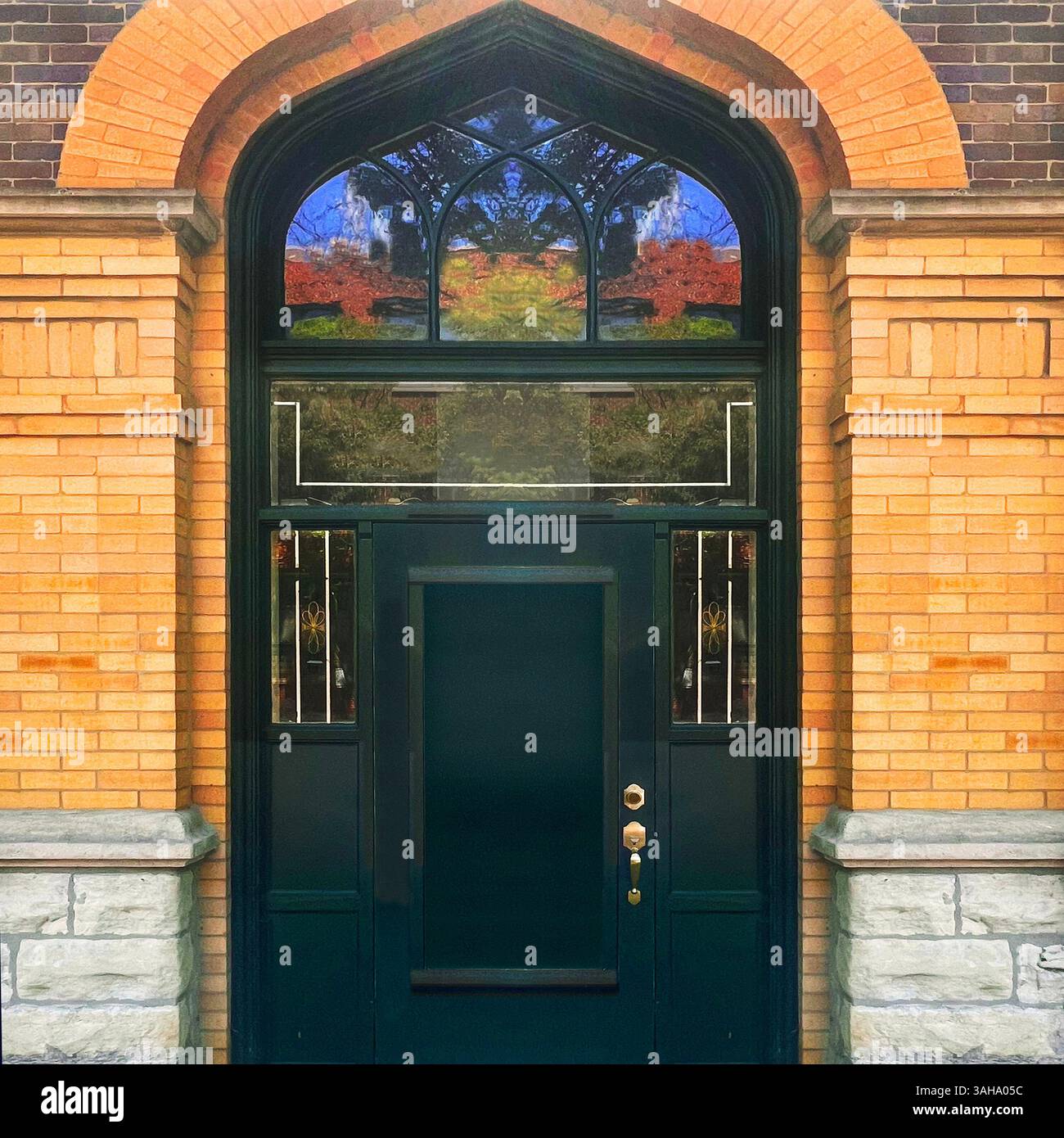 Tiefgrüne Tür in einem gotischen Bogen aus warmen Ziegeln und Stein, eingerahmt von bleihaltigen Fensterakzenten in einem historischen Gebäude in Chicago - Smartphone-aufgenommenes Stockfoto