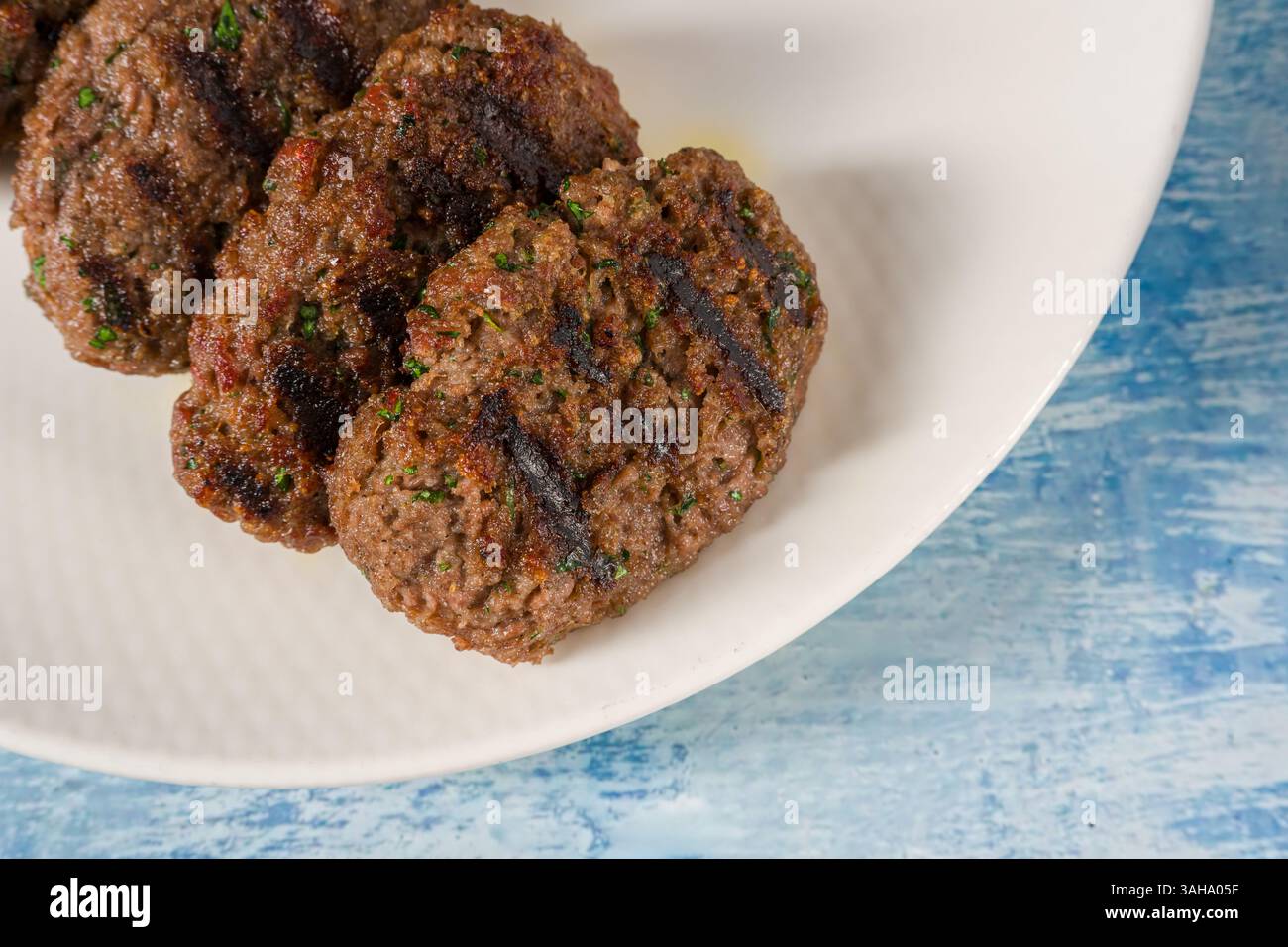 Gegrillte Fleischbällchen auf einem weißen Porzellanteller auf einem blauen Steintisch Stockfoto