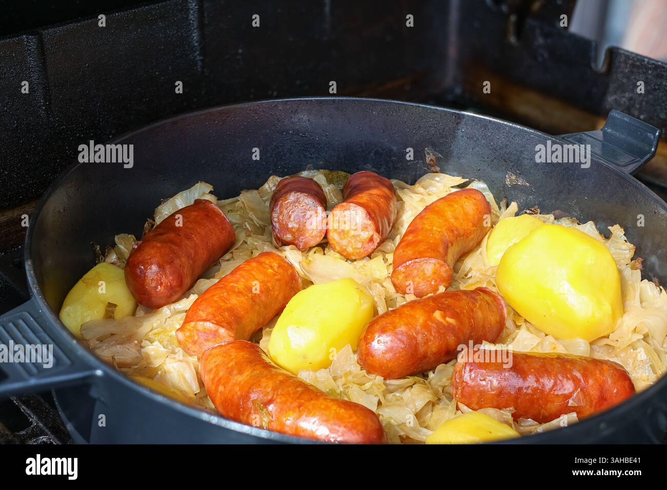 Authentisches und herzhaftes Gericht mit herzhaften Würstchen, ganzen Kartoffeln und gekochtem Kohl, das zusammen in einer Pfanne zubereitet wird. Stockfoto