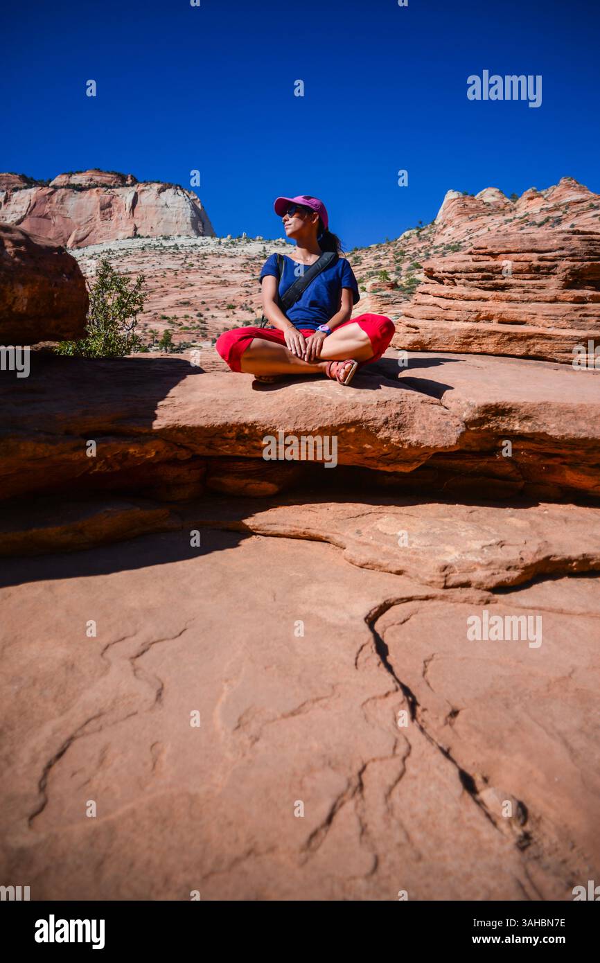 Junge kaukasische Frau sitzt mit überkreuzten Beinen auf dem Canyon Overlook Trail im Zion National Park, Utah Stockfoto
