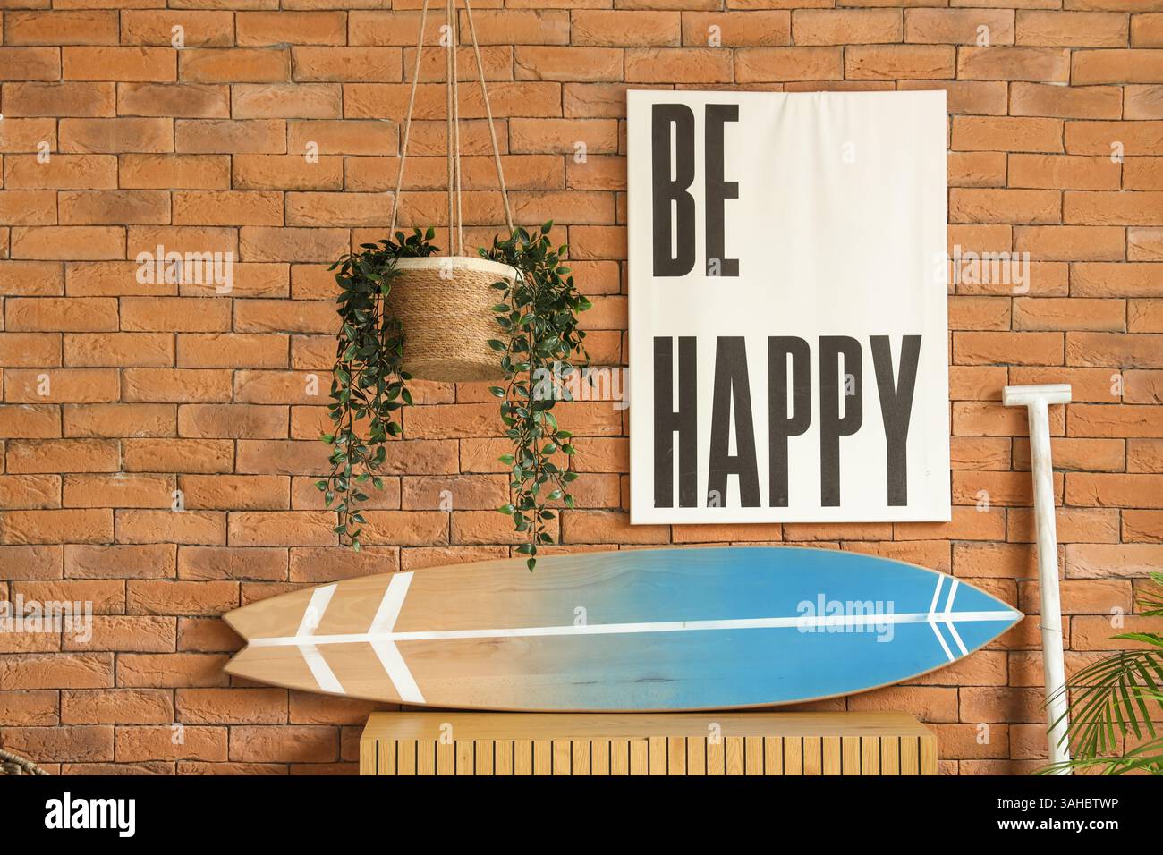 Surfbrett, Paddel und Holzkommode in der Nähe der Ziegelwand Stockfoto