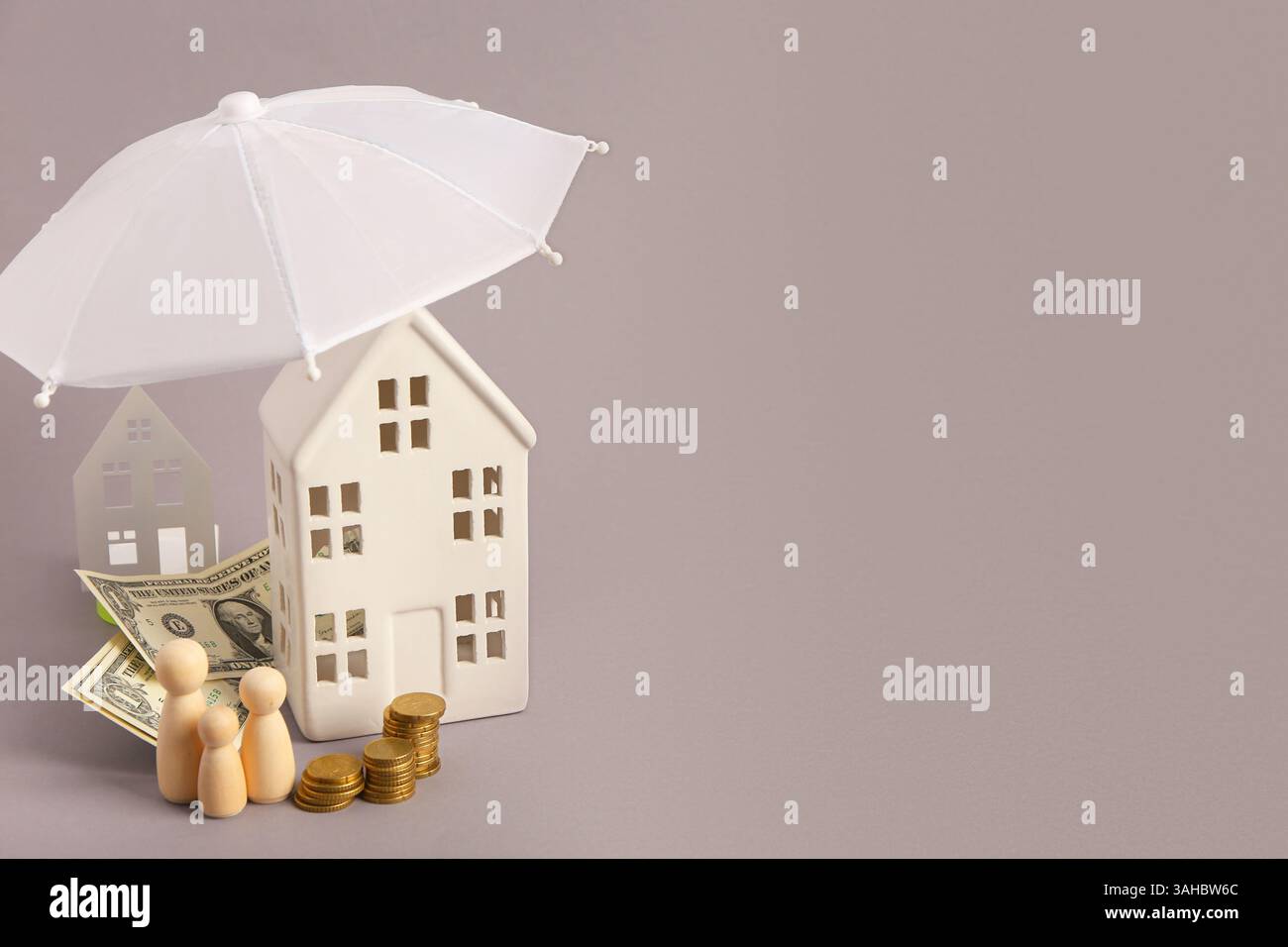 Komposition mit dekorativem Haus, Minischirm, Geld und Holzfiguren der Familie auf grauem Hintergrund Stockfoto