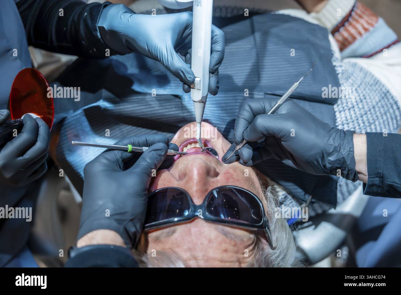 Zahnärzte mit spezieller Ausrüstung führen eine Zahnaufhellung bei einem älteren Patienten in einer modernen Zahnklinik durch Stockfoto