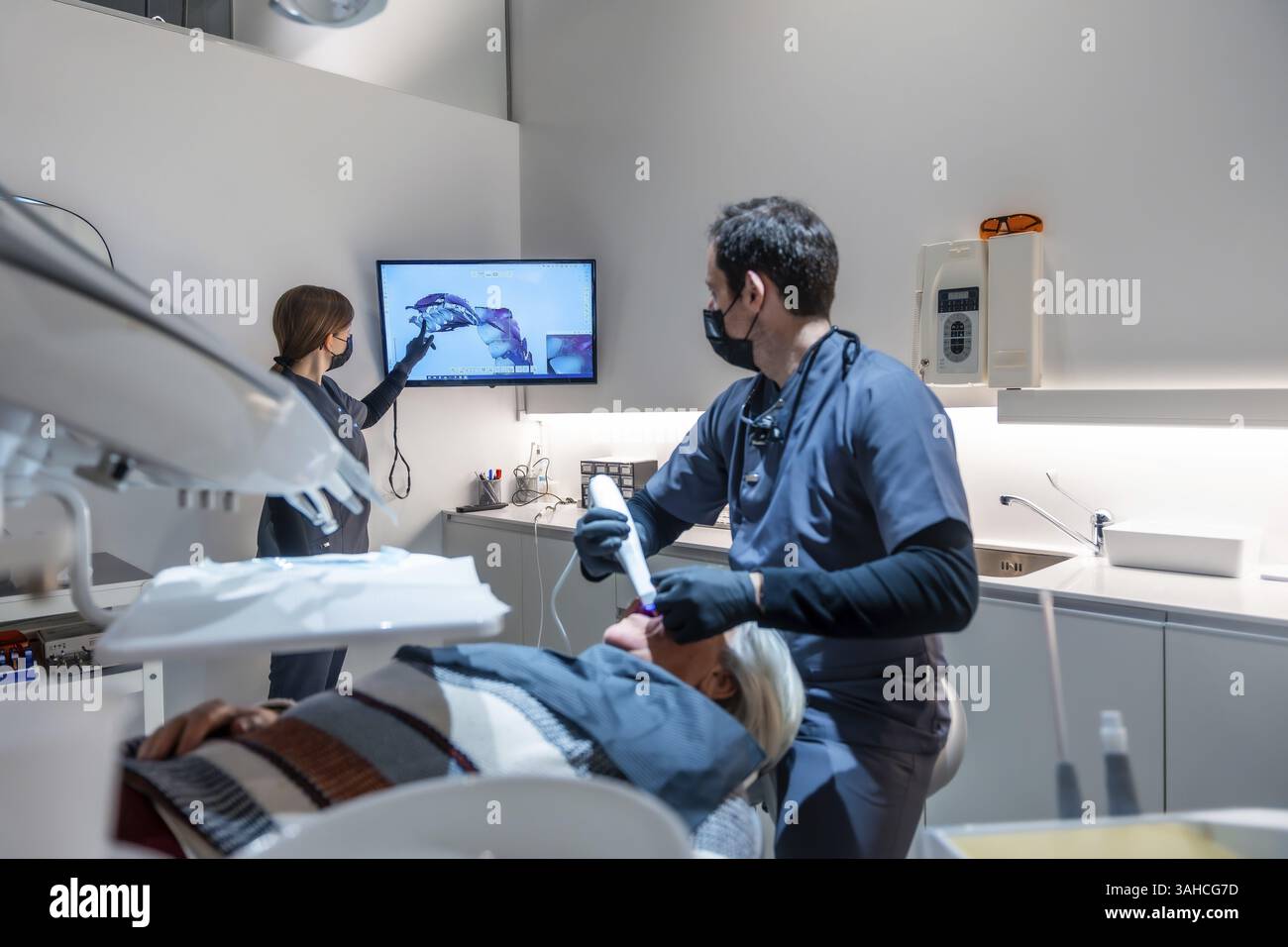 Zahnarztpraxen mit Gesichtsmasken, zahnärztlicher Ausrüstung und dem Patienten während einer Behandlung in einem modernen cli ein Zahnröntgenbild am Monitor zeigen Stockfoto
