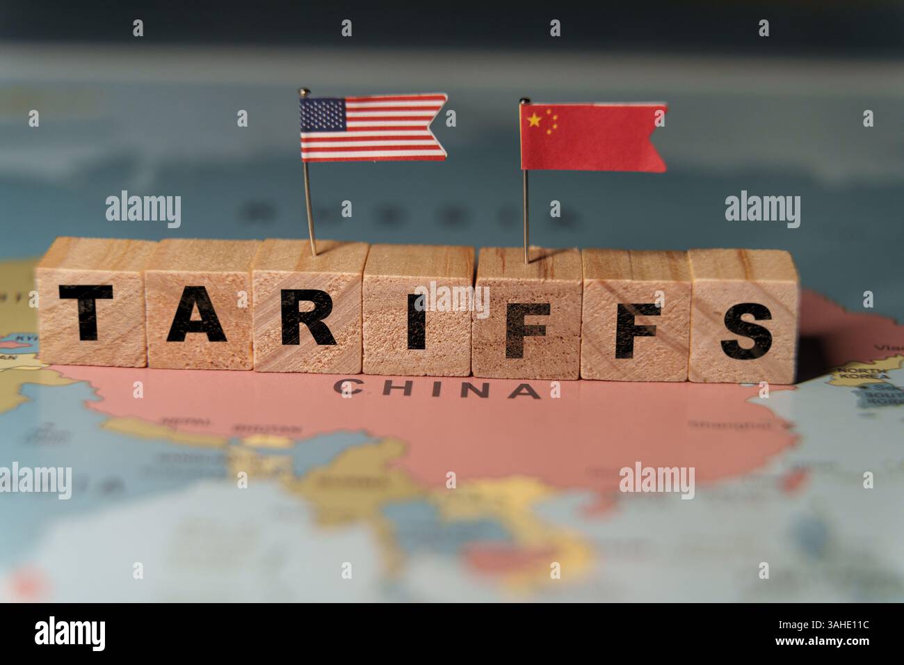 Holzblöcke, die das Wort ZÖLLE auf einer Weltkarte über China bilden, mit kleinen US- und China-Flaggen, die Handelspolitik repräsentieren Stockfoto