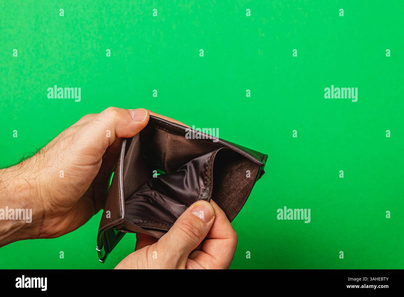 Ein Mann hält eine leere Ledertasche und offenbart die düstere Realität der finanziellen Not. Sein Ausdruck spiegelt die Verzweiflung wider, während er sich mit wachsenden Expens konfrontiert sieht Stockfoto