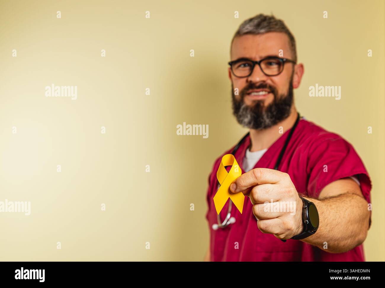 Eine männliche Krankenschwester in Peelings hält ein gelbes Band und lächelt, während er das Gesundheitsbewusstsein fördert. Der Hintergrund ist ein sanfter Farbton, der sein Engagement für p Stockfoto