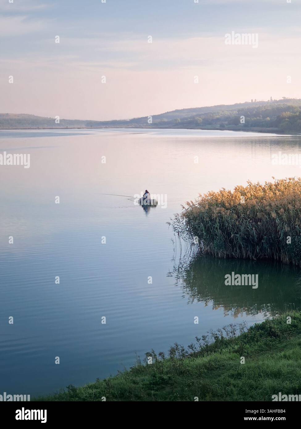Ruhige Szene mit einem Fischer in einem Boot auf dem See, der am frühen Morgen fischt - Smartphone-aufgenommenes Stockfoto
