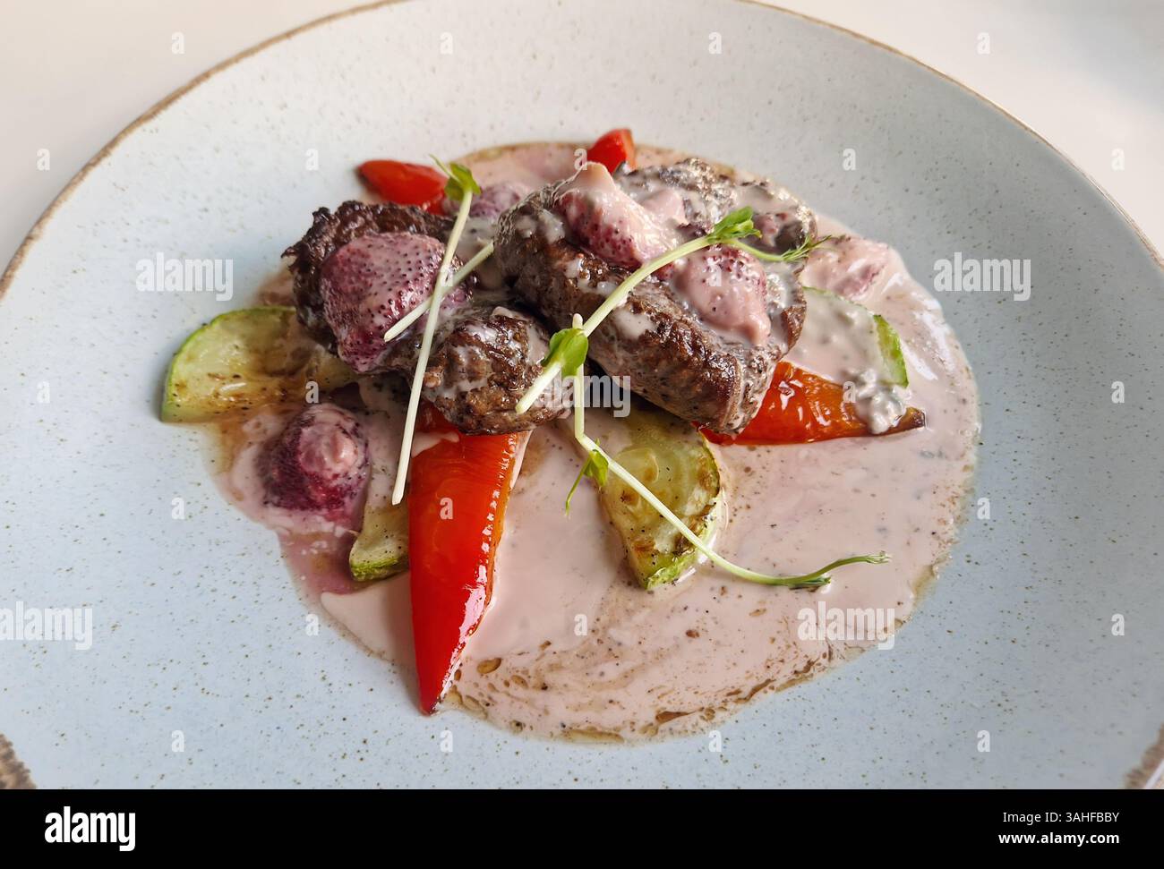 Gegrillte Rindersteak-Medaillons mit weißer Sahnesauce, balsamischen Erdbeeren, Zucchini und Paprika. Nahaufnahme leckeres Essen auf dem Tisch in einem Teller - Smartphone-aufgenommenes Stockfoto