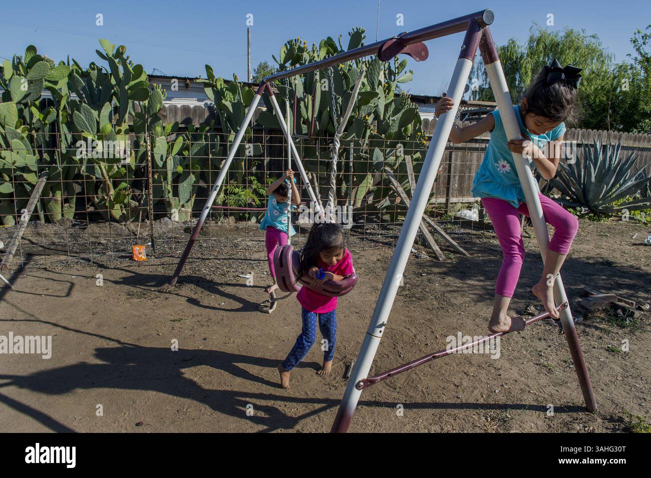 Way of Life Withers in California’s Parched Citrus Belt 27. April 2015 – Monson, Kalifornien, USA – Ignacio Avilas Enkel RENAE AVILA, 4, Center, und Zwillinge DANAE AVILA, 6, links, und DENALIE AVILA, 6, 6, richtig, Spiel auf einer Schaukel in seinem Garten. Avila sagt, dass er recyceltes Wasser für seinen Kaktus verwendet und daher keinen Rasen oder Garten mehr hat. „Dieser Ort war so schön, wie ein Park, nur grün, grün, grün“, sagte Avila. "Jetzt ist es eine Wüste." (Credit Image: © Renee C. Byer/Sacramento Bee/zReportage.com Via ZUMA Press)Way of Life Withers in California’s parched Citrus Belt Stockfoto