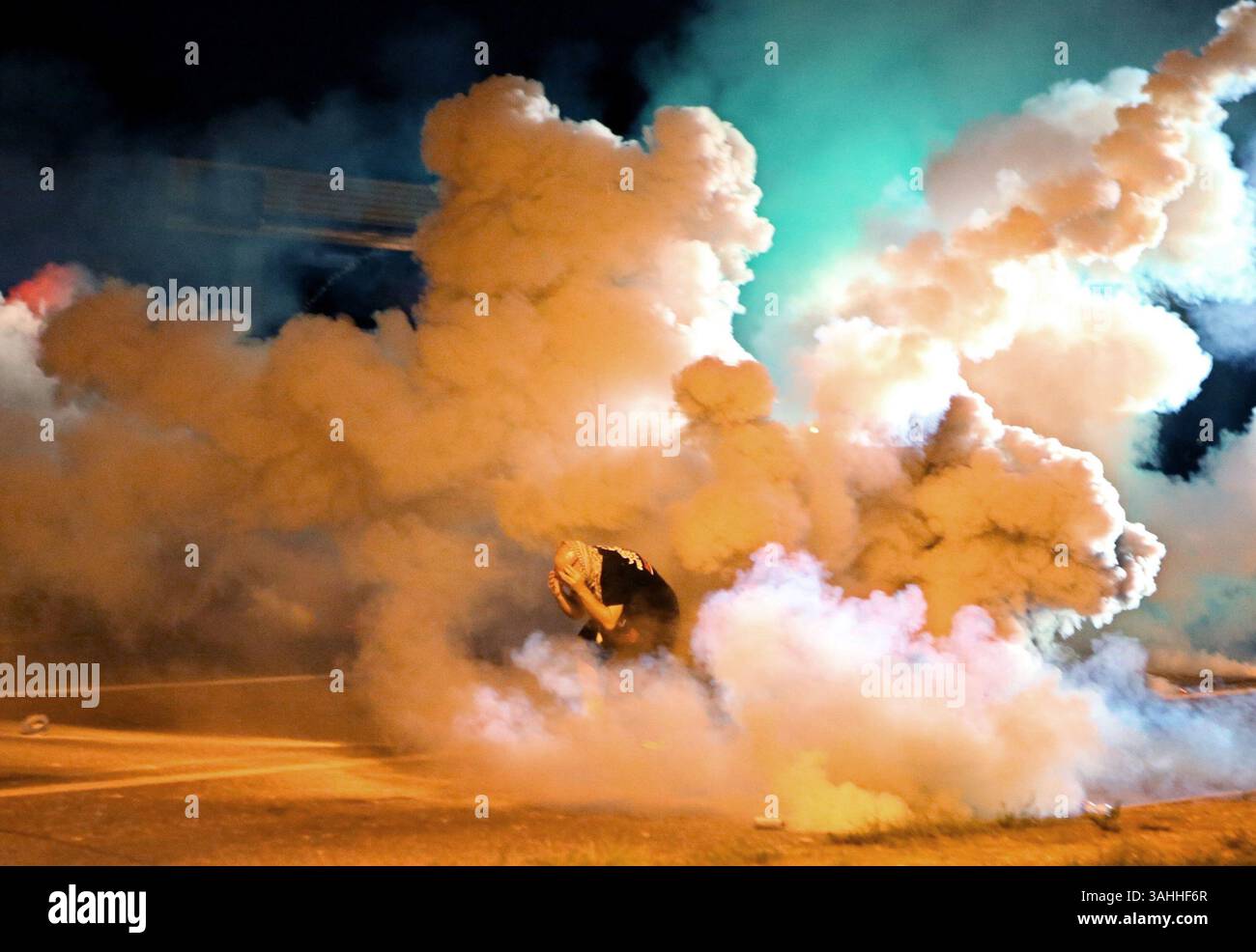 13. August 2014 - Ferguson, Missouri, USA - Ein Demonstrant beschützt sich vor Tränengaskanistern, die um ihn herum auf der West Florissant Avenue explodieren. In dieser Nacht versuchten Demonstranten, Molotow-Cocktails, Steine und Flaschen auf die Polizei zu werfen. Das war die vier nächtlichen Polizisten, die Tränengas benutzten, um Menschenmassen zu zerstreuen, die gegen den Tod von Michael Brown protestierten. (Bild: © David Carson/St Louis Post-Dispatch/ZUMAPRESS.com) Stockfoto