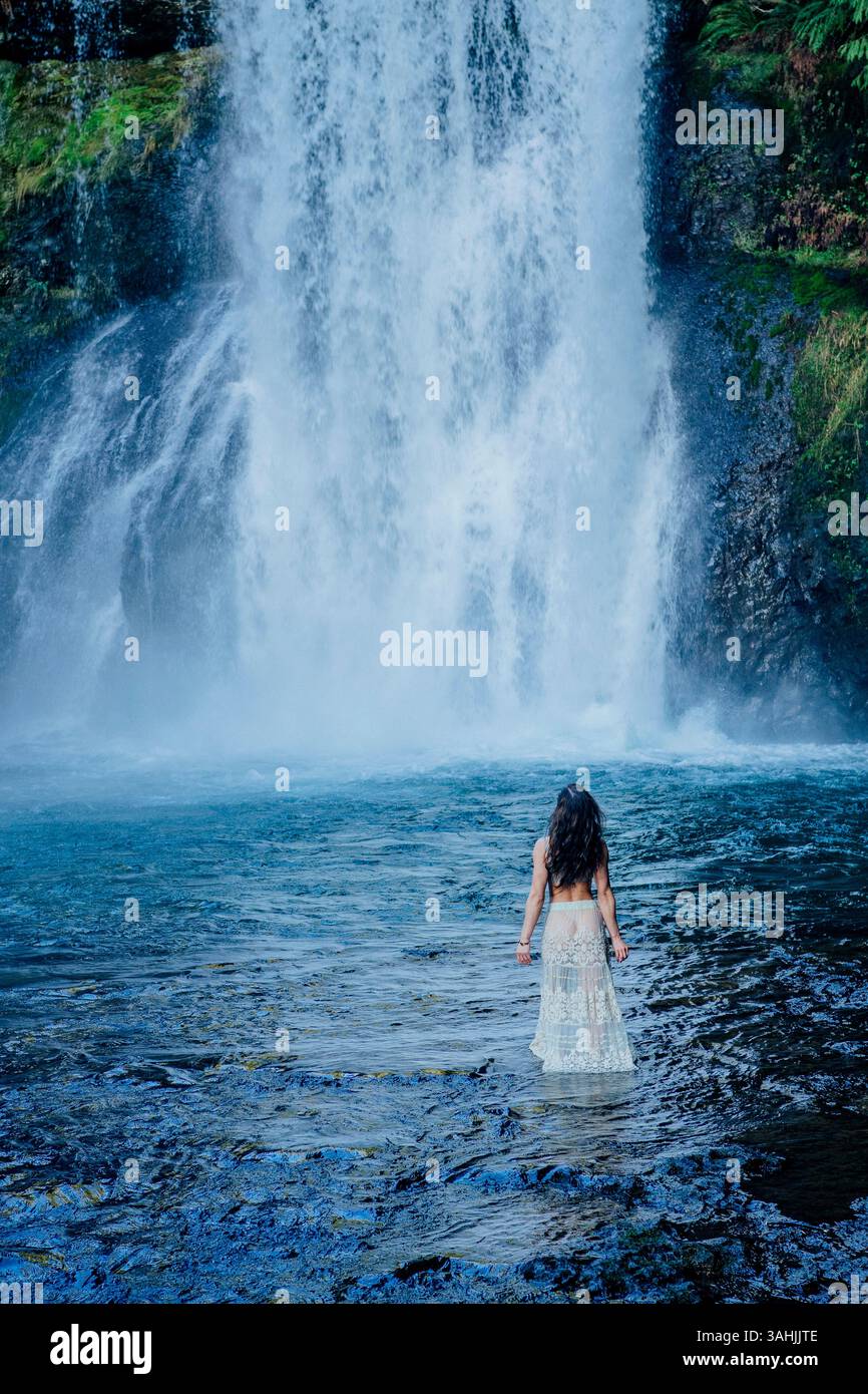 Frau in einem langen Rock im Wasser, mit Blick auf einen großen Wasserfall in einer üppigen, natürlichen Umgebung. Silver Falls, Oregon, USA Stockfoto
