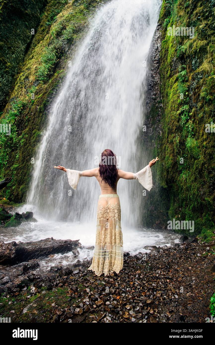 Frau in langem Kleid steht mit ausgestreckten Armen vor einem großen Wasserfall. Silver Falls, Oregon, USA Stockfoto