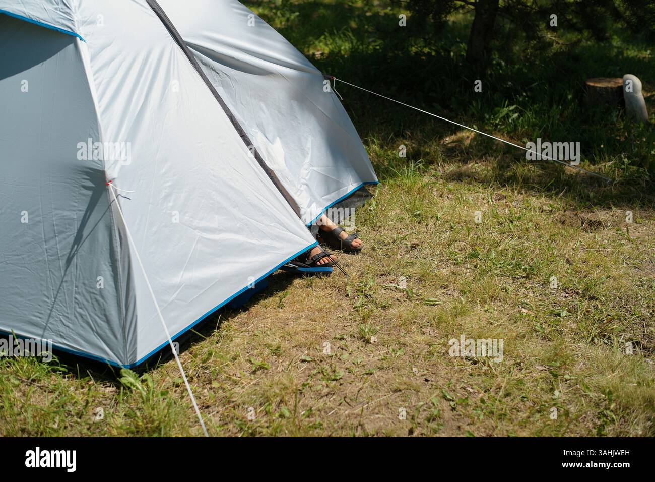Füße in Sandalen blicken aus einem blau-weißen Zelt auf einem grasbewachsenen Campingplatz. Frankreich Stockfoto
