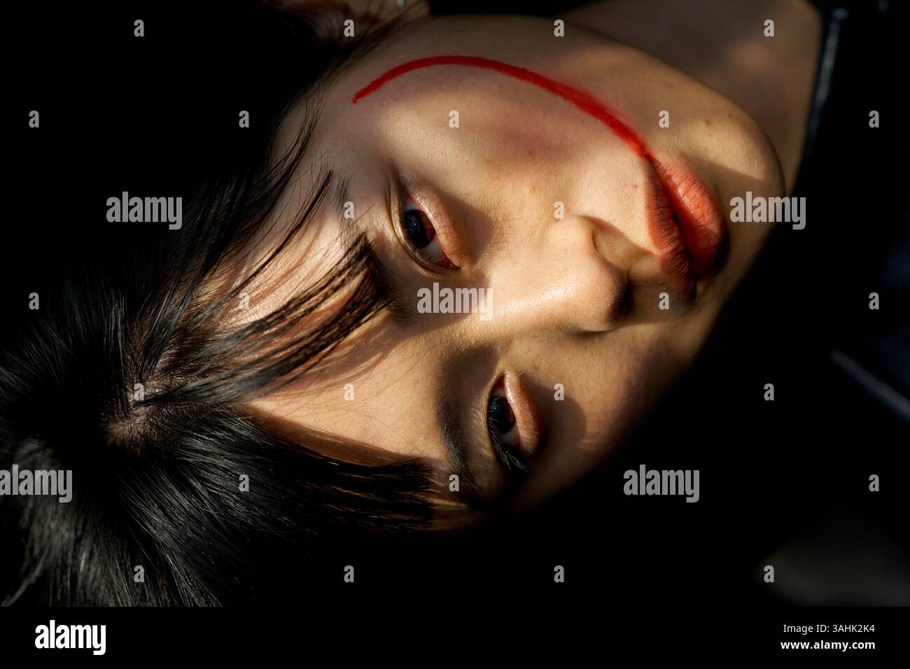 Frau, die mit einem roten Streifen auf der Wange liegt, beleuchtet von sanftem Licht und Schatten. Brandenburg, Deutschland Stockfoto