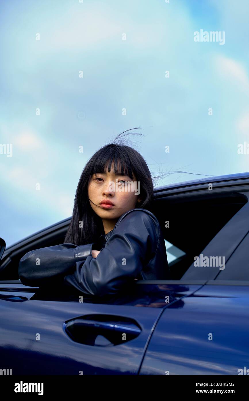 Frau in schwarzer Jacke lehnt sich aus dem Autofenster vor einem bewölkten Himmel. Brandenburg, Deutschland Stockfoto