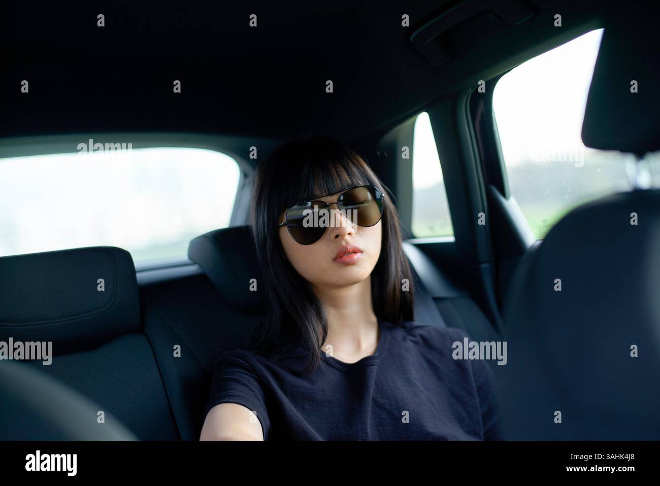 Frau mit Sonnenbrille sitzt hinten im Auto und blickt ruhig aus dem Fenster. Brandenburg, Deutschland Stockfoto