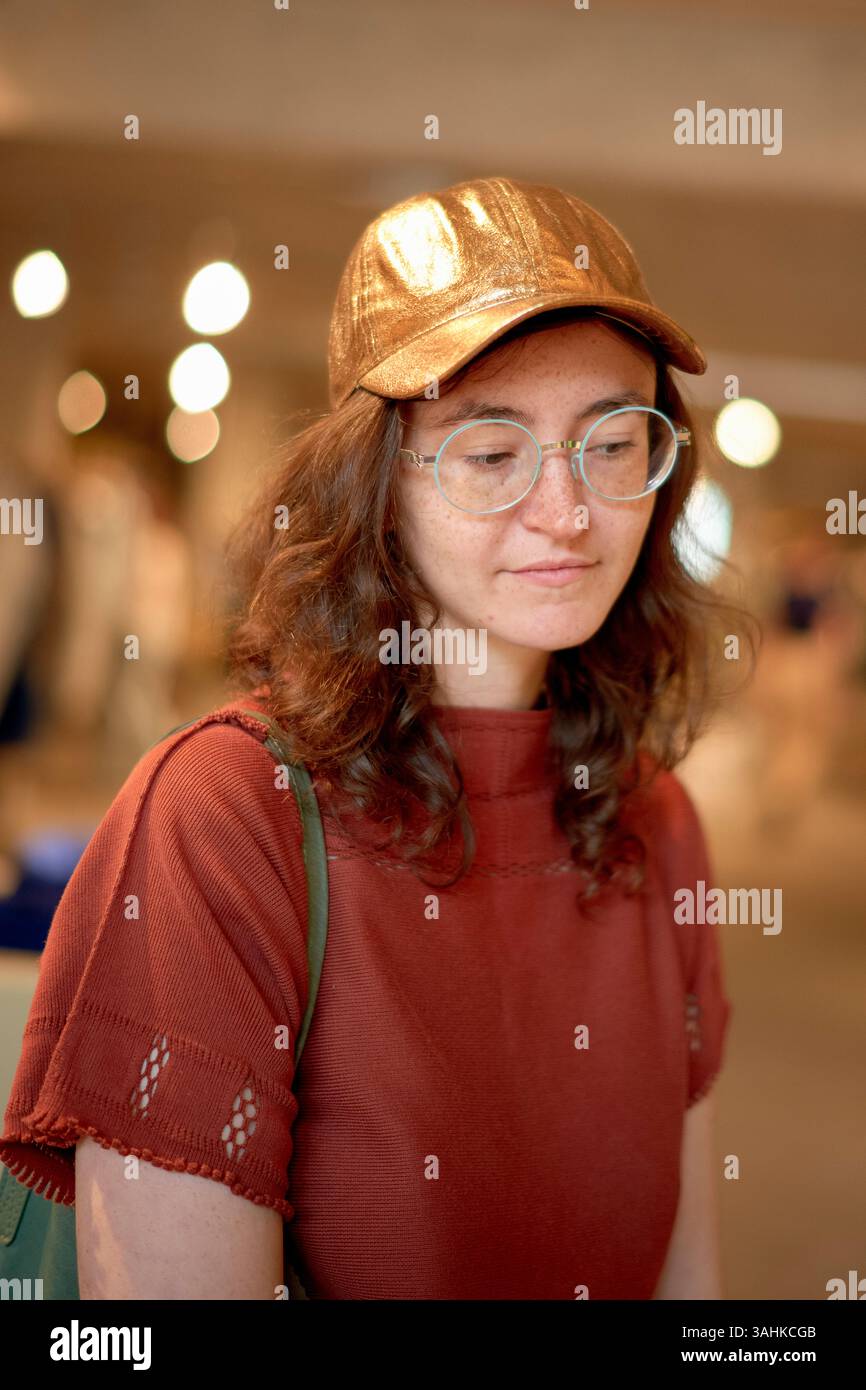 Frau in rotem Hemd und goldener Mütze mit Brille im Innenbereich beim Einkaufen. Stockfoto