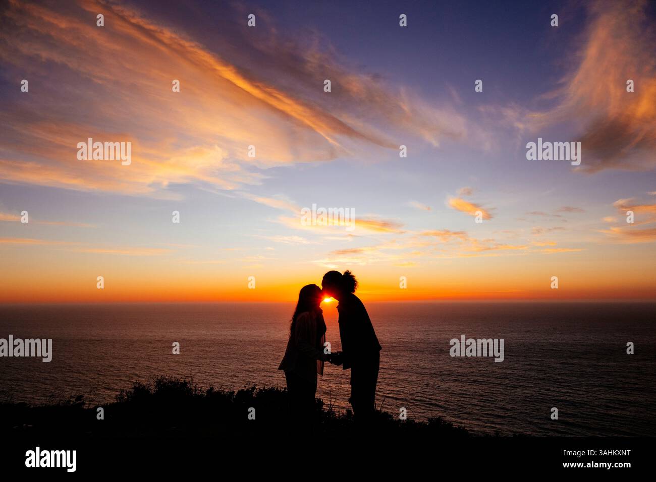 Romantisches Paar mit einer Silhouette bei Sonnenuntergang auf einer Klippe mit Blick auf das Meer. Monterey, CA, USA Stockfoto Romantisches Paar mit einer Silhouette bei Sonnenuntergang auf einer Klippe mit Blick auf das Meer. Monterey, CA, USA Stockfoto