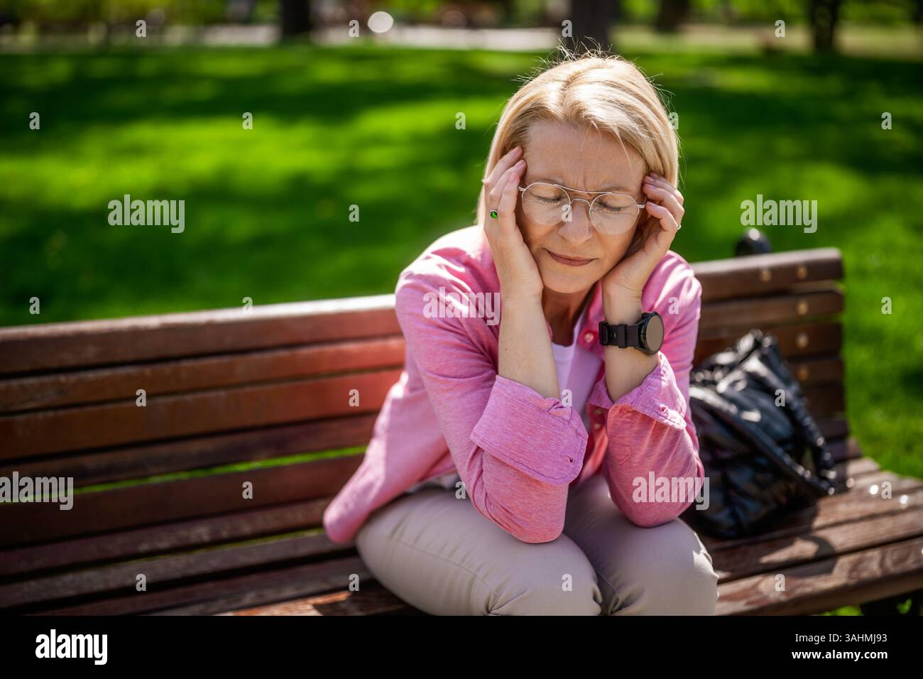 Die nachdenkliche reife Frau sitzt an sonnigen Tagen auf einer Bank im Park. Stockfoto