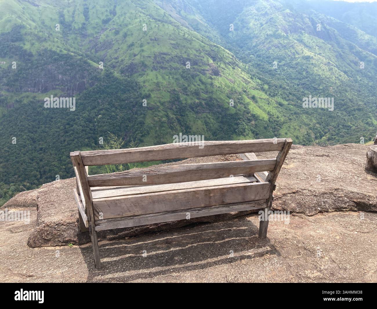 Eine hölzerne Bank auf felsigen Höhen, umgeben von Bäumen und ruhiger Brise, ist der perfekte Ort, um zu pausieren und zu atmen. - Smartphone-aufgenommenes Stockfoto