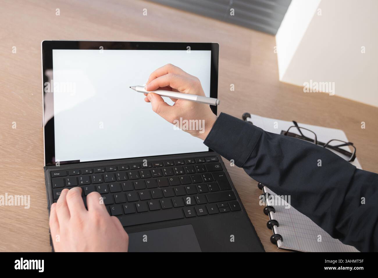 Ein erfahrener Fachmann verwendet einen digitalen Stift aktiv auf einem schlanken Laptop in einer modernen Arbeitsumgebung Stockfoto