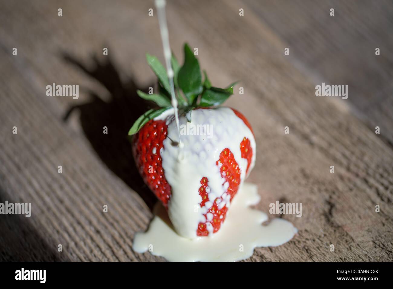Einzelne Erdbeere (Fragaria x Ananassa) mit Creme auf rustikalem Holz, symbolisiert Sommerdesserts, Genießen und frische saisonale Speisen Stockfoto