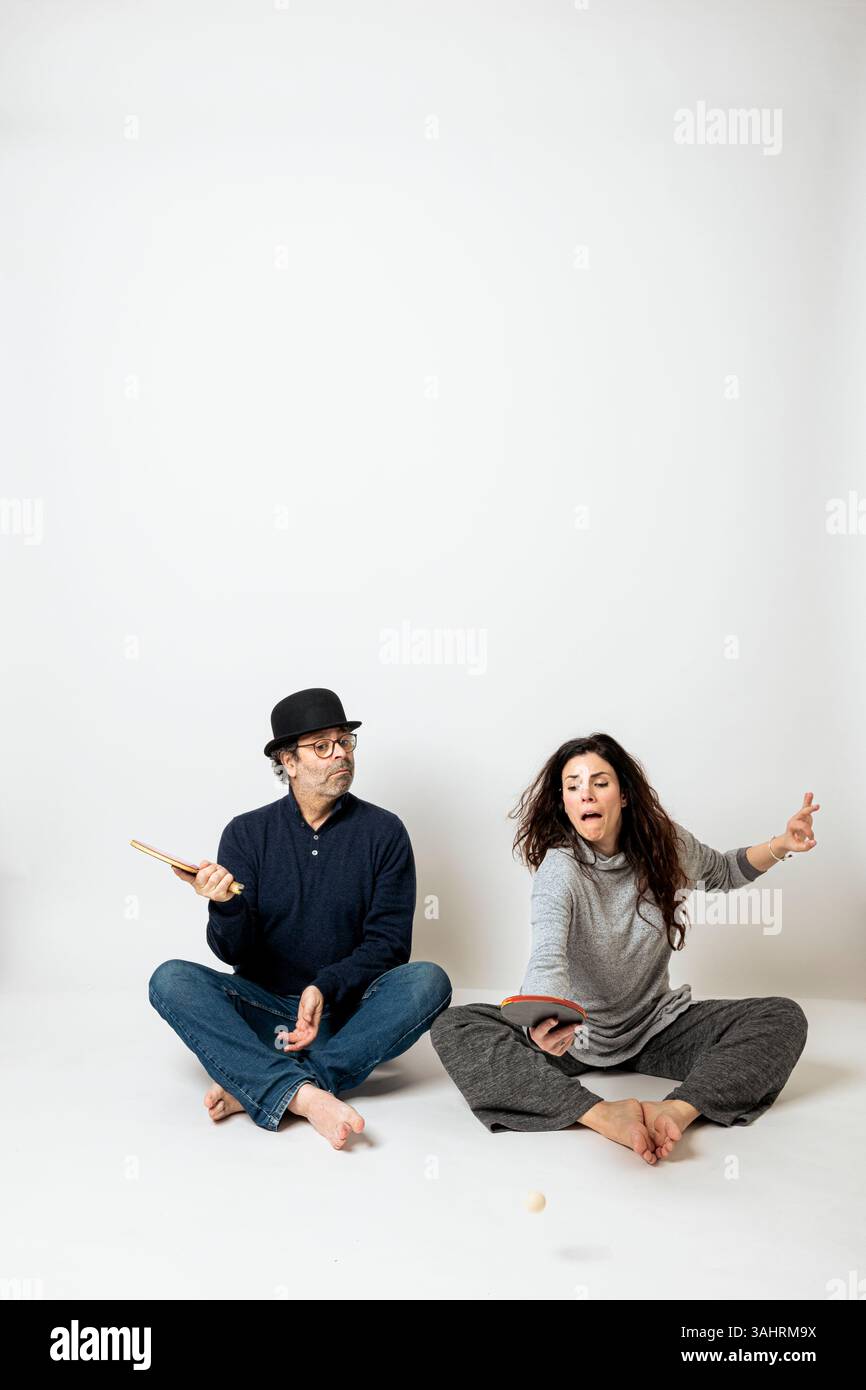 Ein Mann und eine Frau spielen Tischtennis, haben den Ball in die Luft geworfen und sehen ihn amüsant an. Isolierte Szene auf weißem Hintergrund Stockfoto