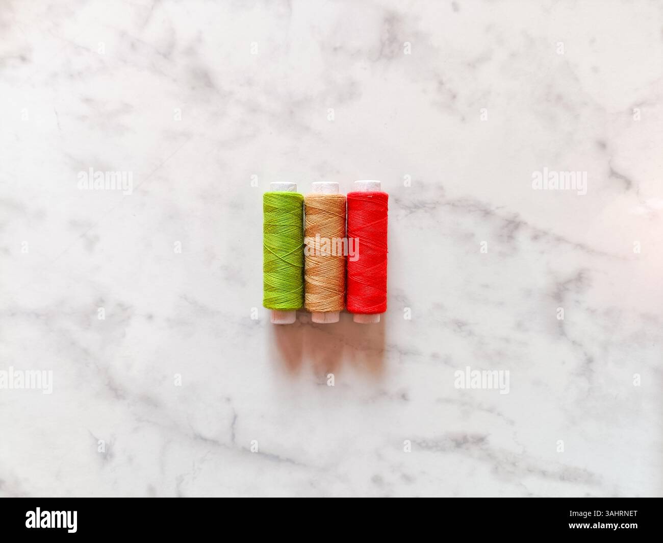 Drei farbenfrohe Garnspulen auf einem glatten weißen Marmorhintergrund. Das Gewinde befindet sich in der Mitte, sodass am Rand genügend Platz bleibt - Smartphone-aufgenommenes Stockfoto