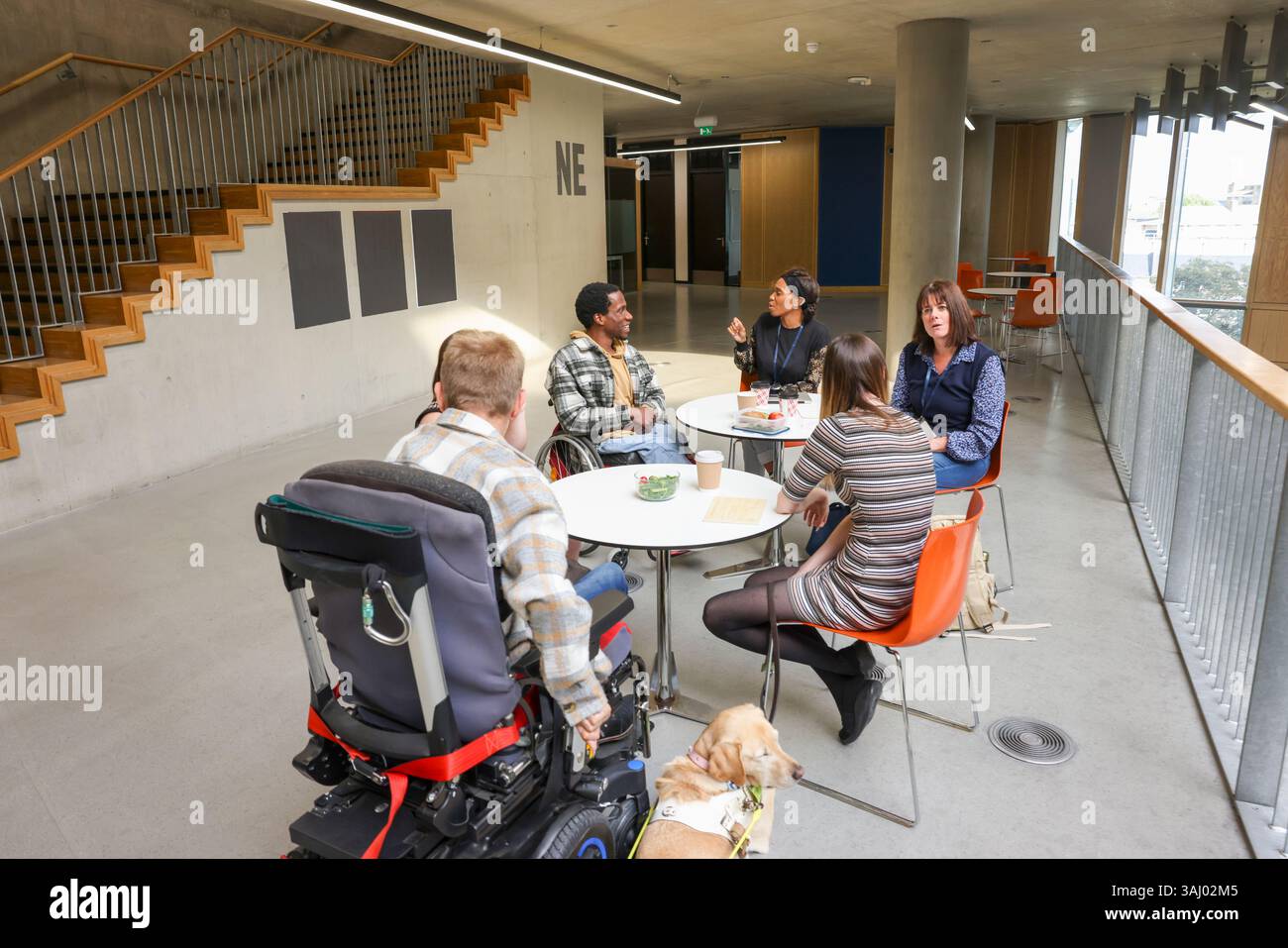 Menschen mit verschiedenen Behinderungen an Tischen im Flur Stockfoto