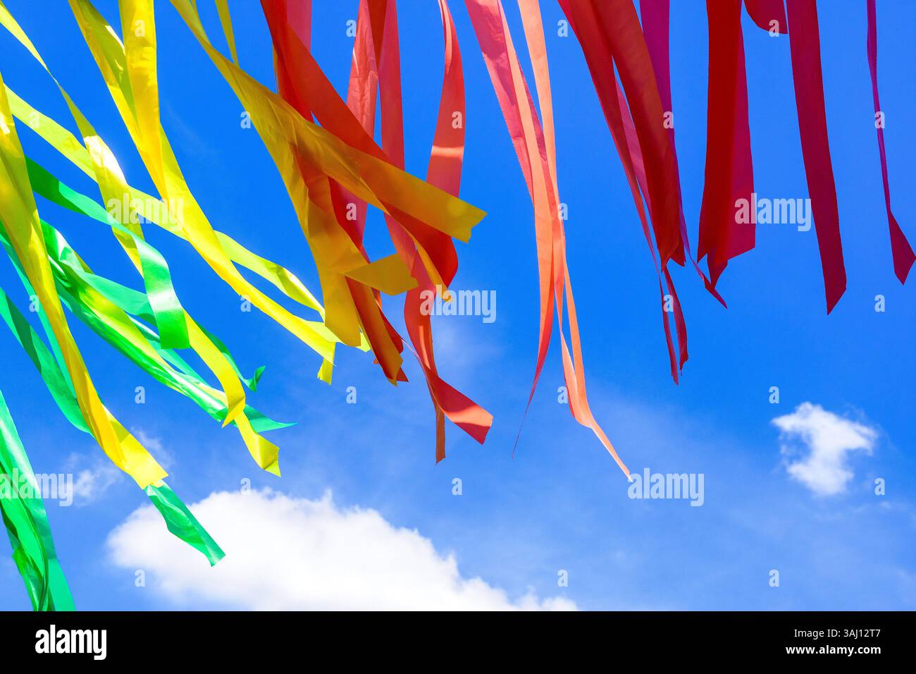 Grüne, gelbe, orange und rote Plastikbänder, die im Wind vor blauem Himmel aufblühen. Stockfoto
