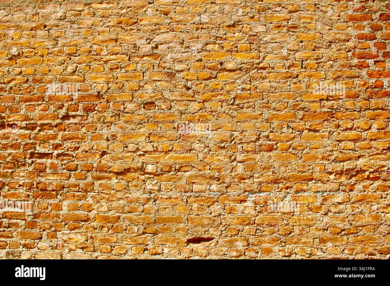 Helle orange und gelbe Ziegelwand, lebendige rustikale Textur, geeignet für Hintergründe und architektonische Designelemente. Stockfoto