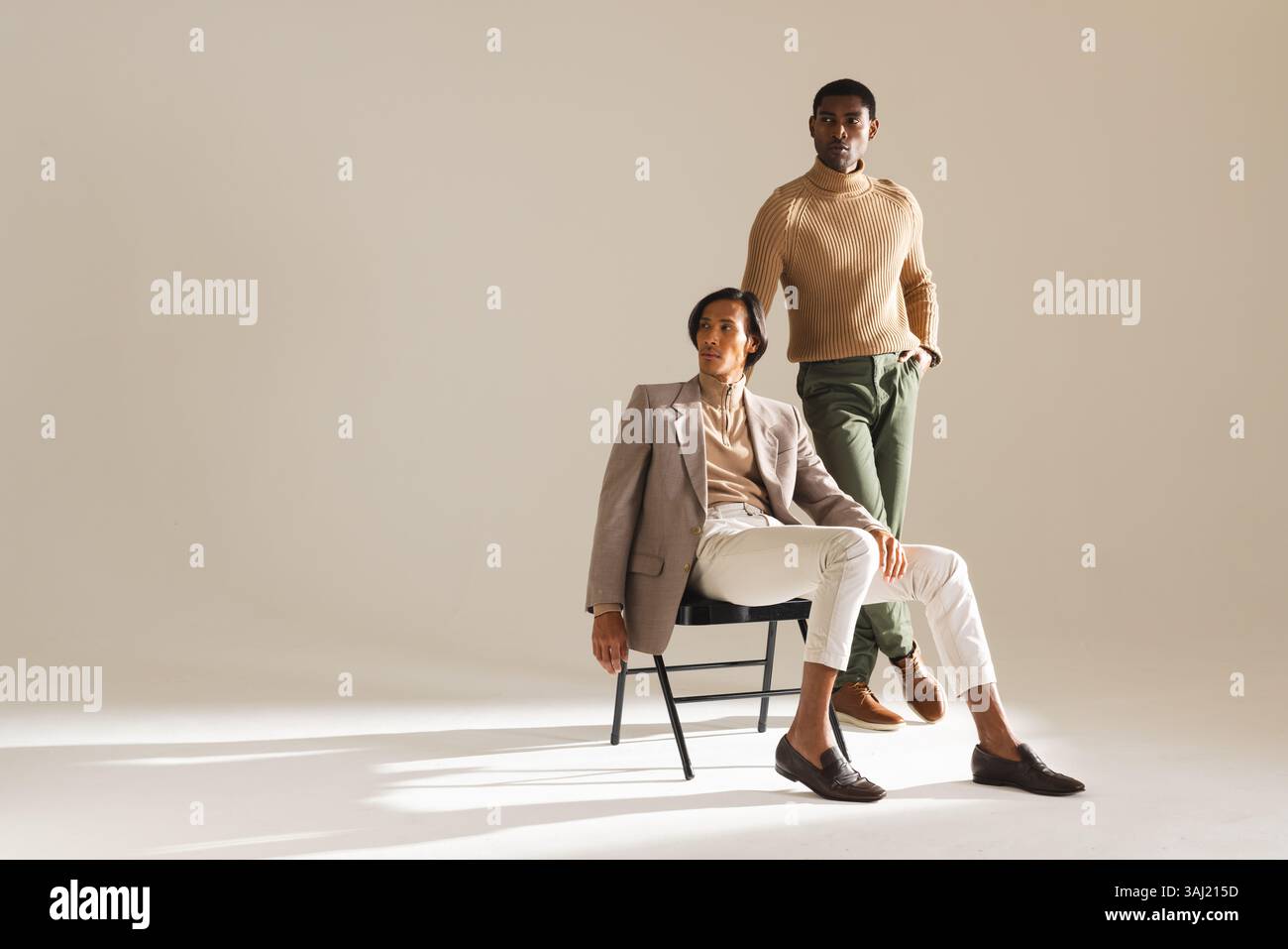 Asiatische und afroamerikanische Models, die im Studio posieren, modische Looks mit schwarzem Stuhl. Mode, Modeling, Minimalismus, Studio, Freizeit, elegan Stockfoto