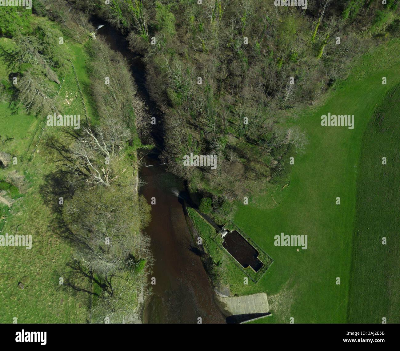 Eine Luftaufnahme von oben zeigt den Fluss, der durch eine lebhafte grüne Landschaft mit Bäumen am Ufer verläuft. In der Nähe des Flusses ist eine kleine Struktur zu sehen Stockfoto