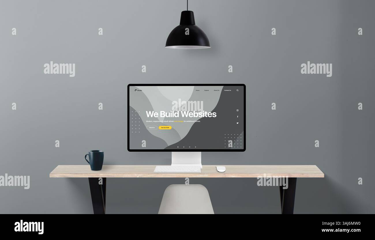 Einfacher Schreibtisch mit Computerdisplay mit Konzeptwebsite für ein Webdesign-Studio, Überschrift „Wir bauen Websites“, graue Wand und Lampe darüber Stockfoto