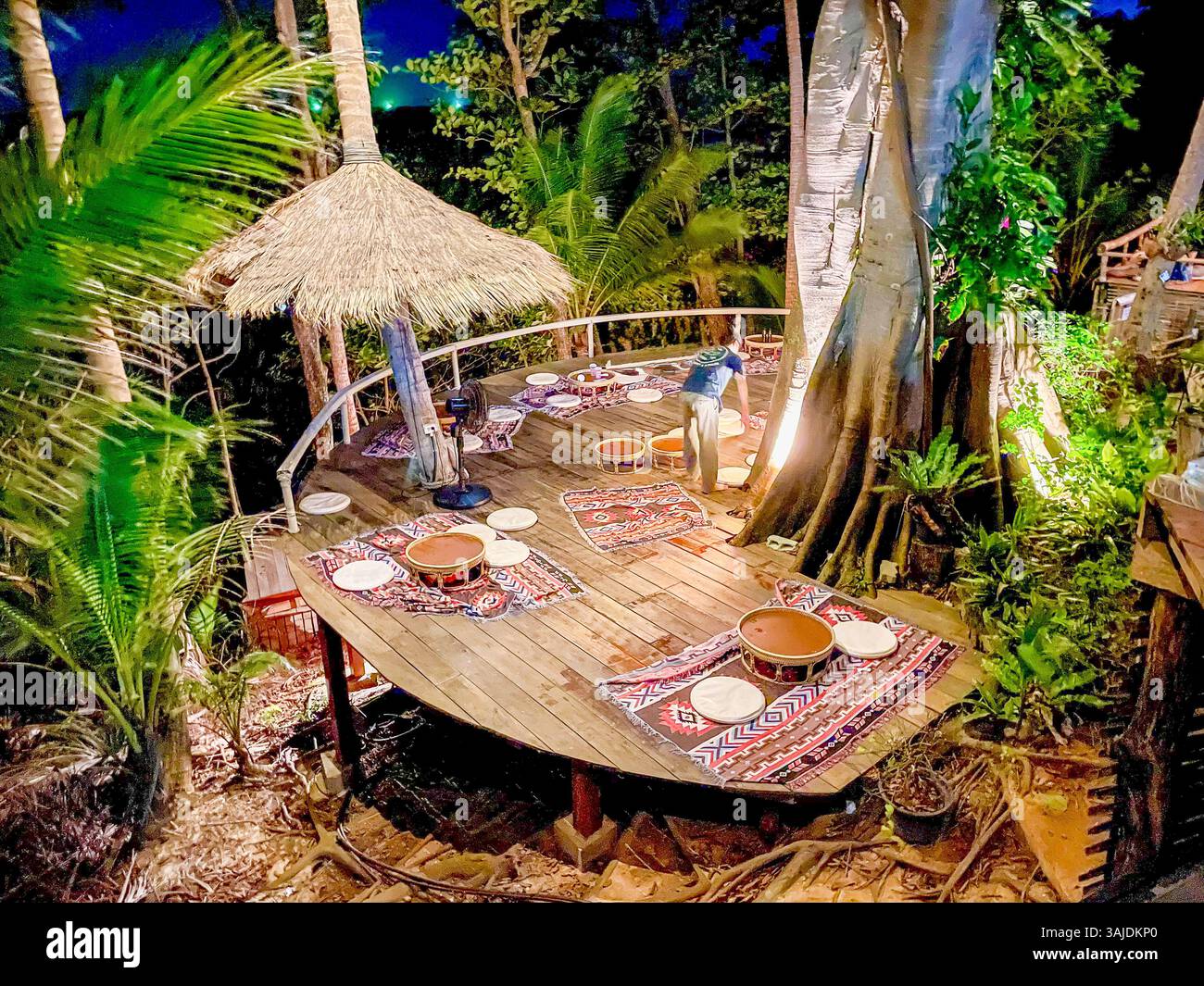 Ein einzigartiger Open-Air-Essbereich im Dschungel mit Holztischen, gewebten Teppichen und gedämpfter Beleuchtung. Die natürliche Umgebung und die gemütliche Atmosphäre c Stockfoto