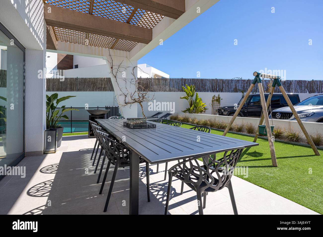 Schattige Terrasse mit großem, modernen Tisch und Stühlen, Blick auf einen kleinen umzäunten Garten. Stockfoto