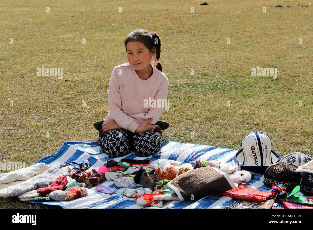 Ein kirgisisches Kind verkauft traditionelle Souvenirs. Das Mädchen verkauft Kunsthandwerk wie Hüte, Socken, Handschuhe, Spielzeug. Stockfoto