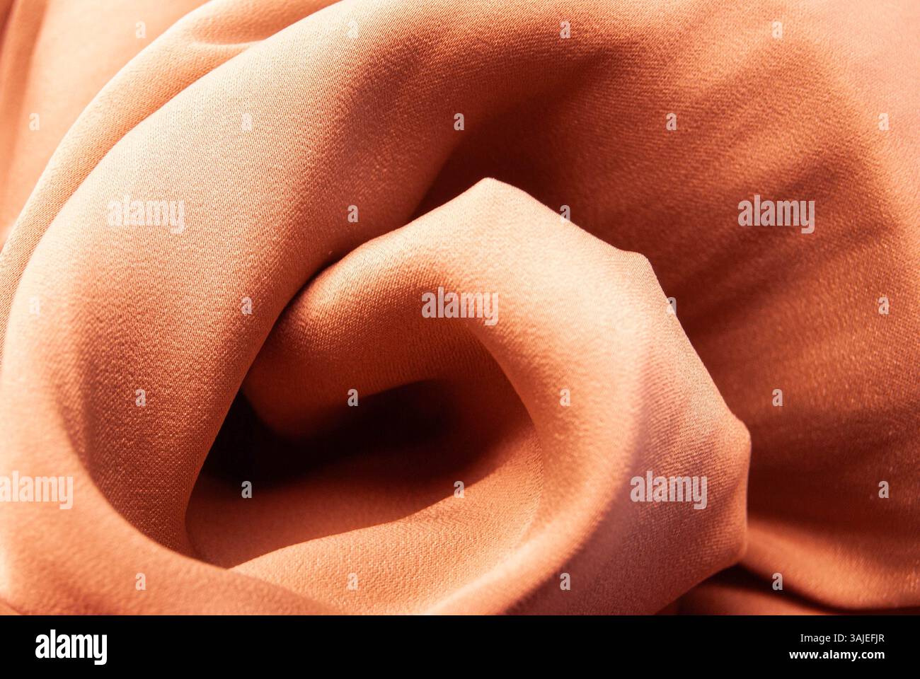 Glatter, orangefarbener Seidenstoff in Pastellfarben mit sanftem Glanz und weichen fließenden Falten für einen warmen und eleganten Hintergrund. Stockfoto