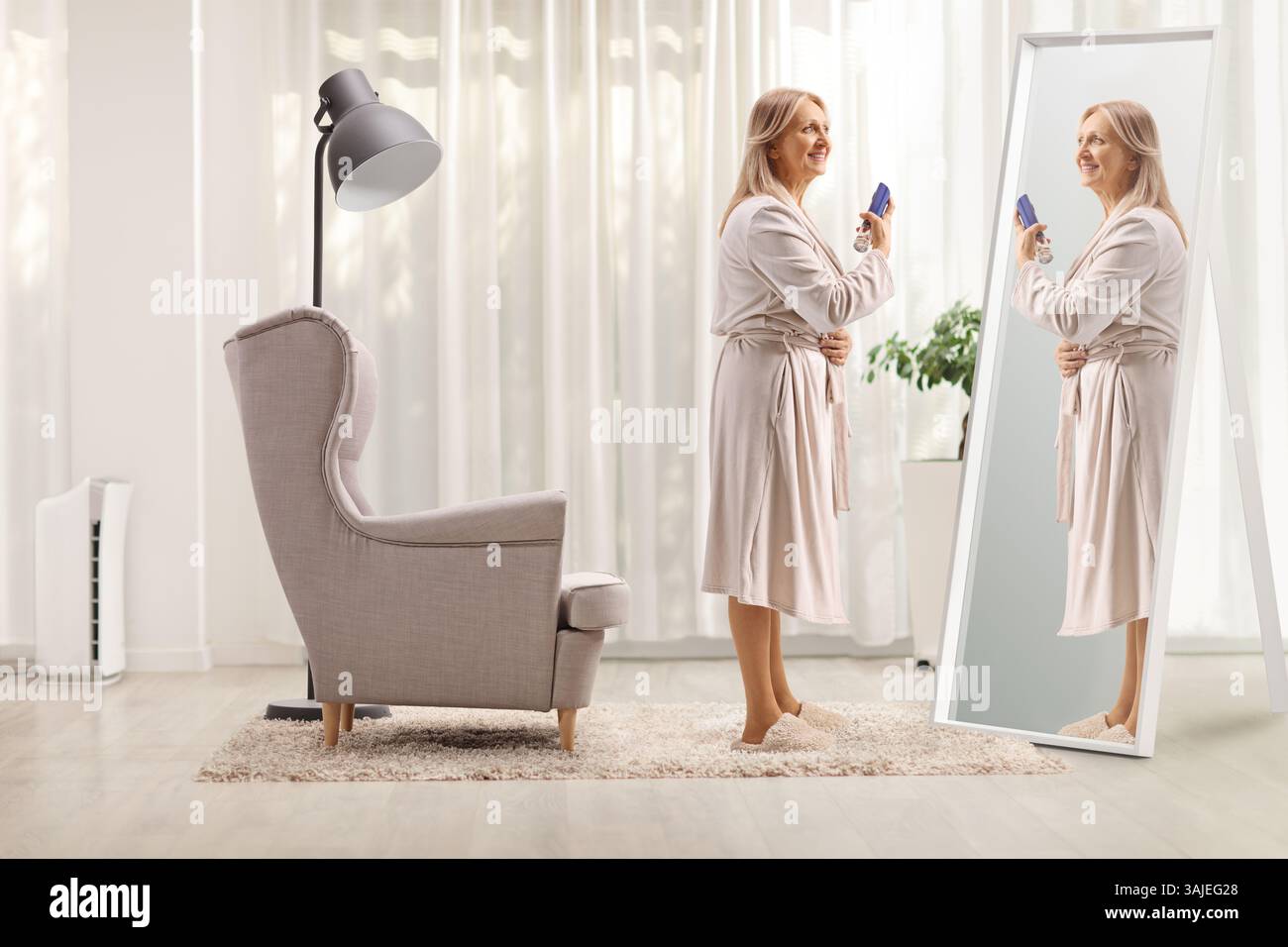 Frau im Bademantel, die zu Hause vor einem Spiegel ein Parfüm sprüht Stockfoto