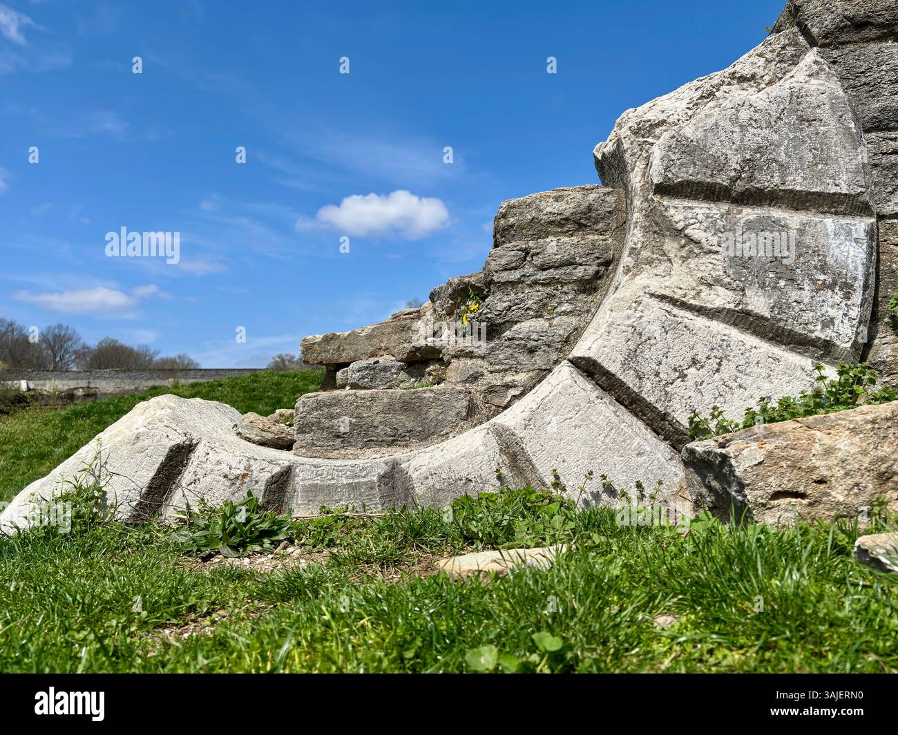 Nahaufnahme von verwitterten Steinbogenruinen umgeben von Gras und Himmel Stockfoto